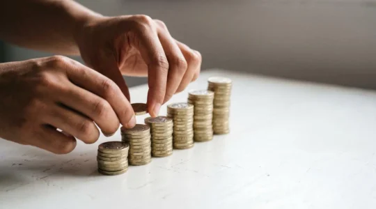 Hands carefully stacking British pound coins in ascending piles against a minimal background, symbolizing building emergency savings during economic uncertainty